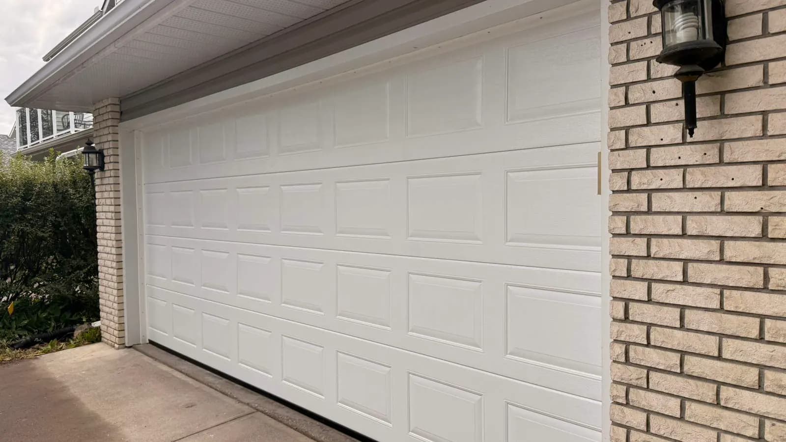 White 16x7 Ryterna Cassette garage door installed on a brick home in Deer Run Calgary